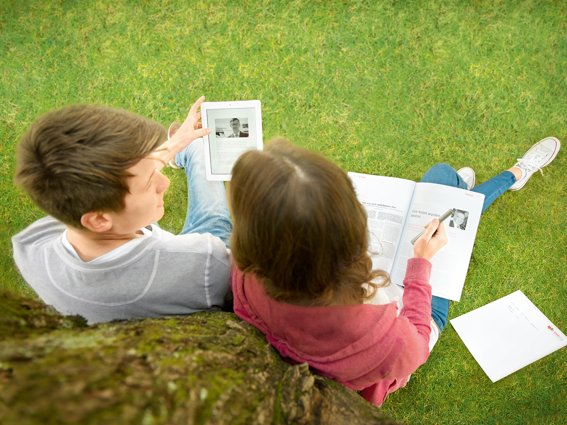 Zwei Studenten sitzen an einem Baum und lesen ein Buch. 