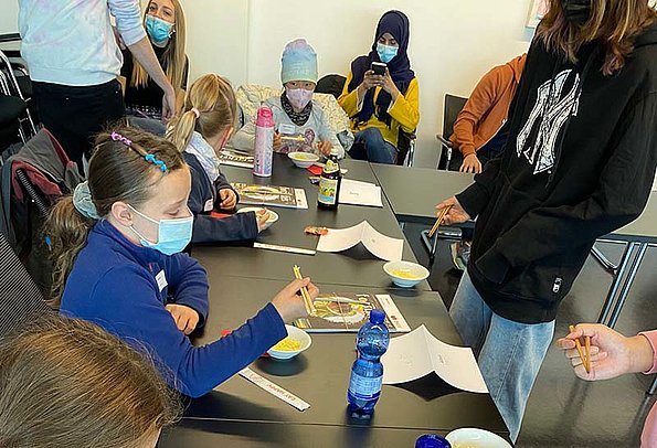 Kinder-Uni 2021 Kurs Multi-Kulti: Kinder lernen, wie man mit Stäbchen essen kann. 