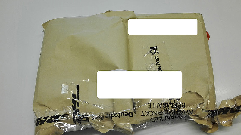 Eine Büchersendung, die in einem einfachen Papierumschlag verpackt ist und der von der Post mit Klebeband zusammengeflickt werden musste.