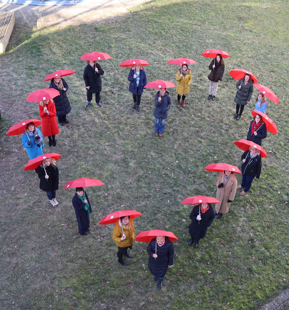 18 Frauen mit roten Regenschirmen bilden ein großes Herz, das von oben fotografiert wurde