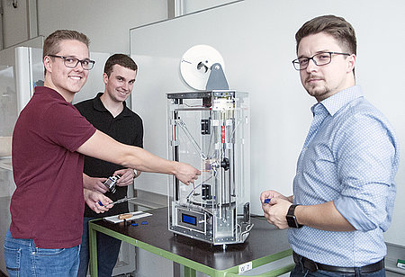 Maschinenbau-Studierende bauen 3D-Drucker Studierende vor ihrem selbst entwickelten 3D-Drucker