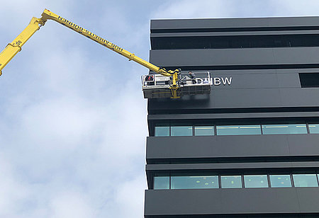 Arbeiter monieren mithilfe eines Krans das Logo der DHBW